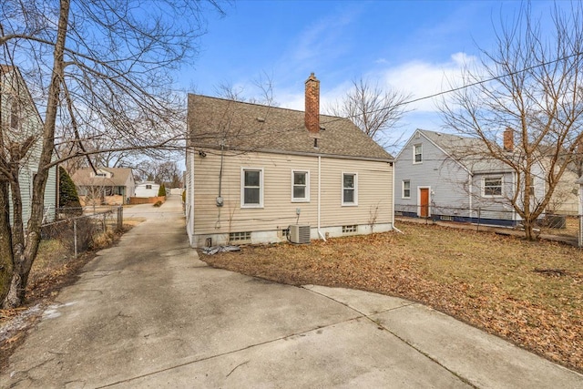 rear view of house with a chimney, fence, central AC, and roof with shingles