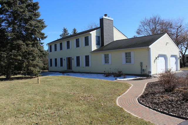 back of house featuring a lawn, a garage, and a chimney