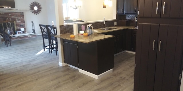 kitchen with a peninsula, wood finished floors, a sink, a brick fireplace, and decorative backsplash