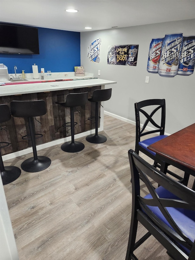 bar with baseboards, bar, light wood-style flooring, a sink, and recessed lighting