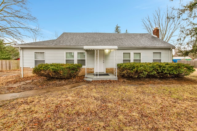 ranch-style home with a chimney, fence, and roof with shingles