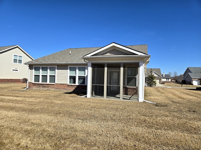 rear view of property with a shingled roof, a sunroom, brick siding, and a yard