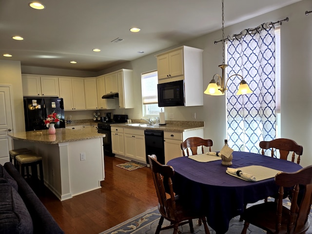 kitchen with under cabinet range hood, a sink, visible vents, black appliances, and dark wood finished floors