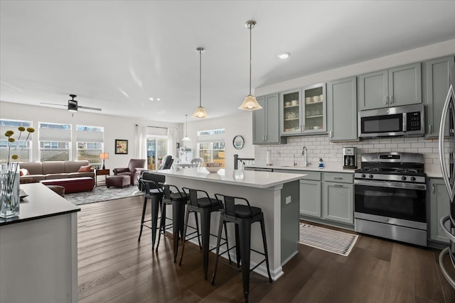 kitchen featuring a breakfast bar, gray cabinets, appliances with stainless steel finishes, open floor plan, and backsplash