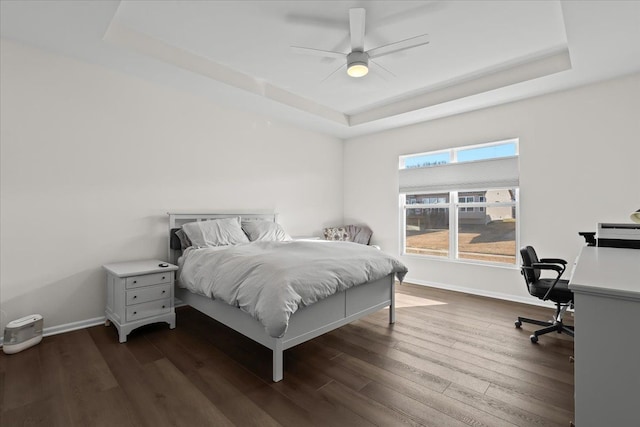 bedroom featuring baseboards, a raised ceiling, dark wood finished floors, and a ceiling fan