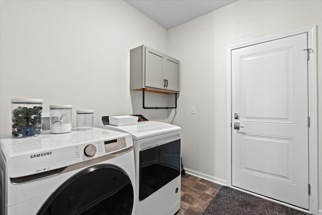 washroom featuring stone finish floor, cabinet space, baseboards, and washing machine and clothes dryer