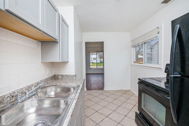 kitchen featuring light tile patterned floors, a sink, light countertops, black appliances, and backsplash