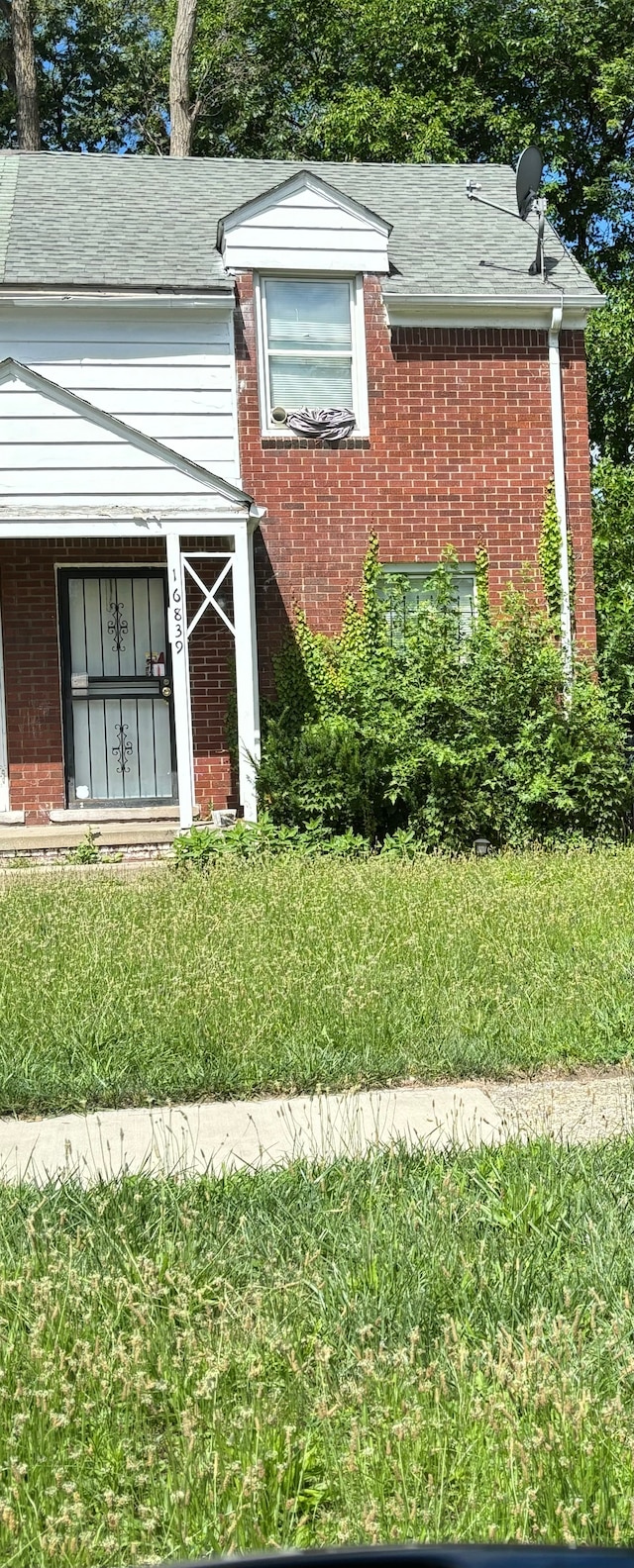 view of property exterior featuring a yard, roof with shingles, and brick siding