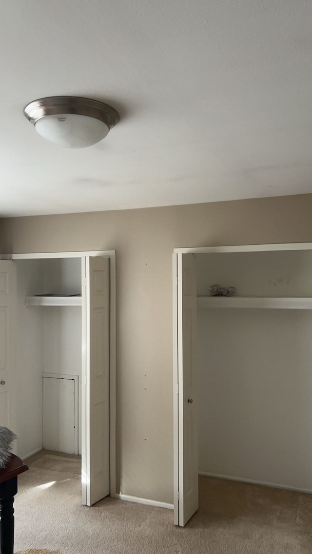 unfurnished bedroom with light carpet, baseboards, and two closets