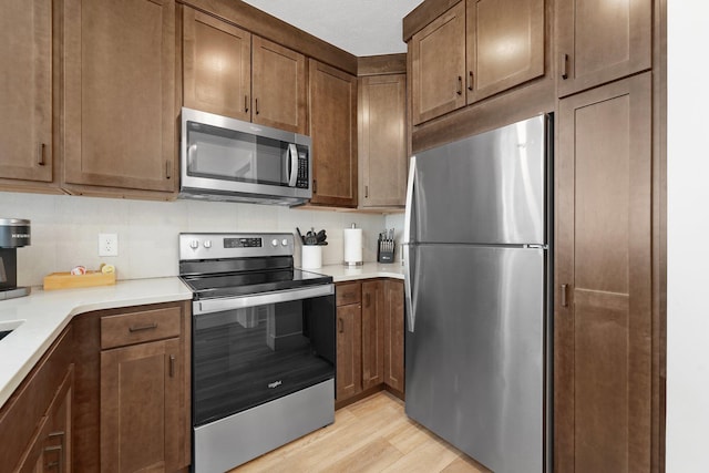 kitchen featuring stainless steel appliances, light wood-type flooring, light countertops, and decorative backsplash