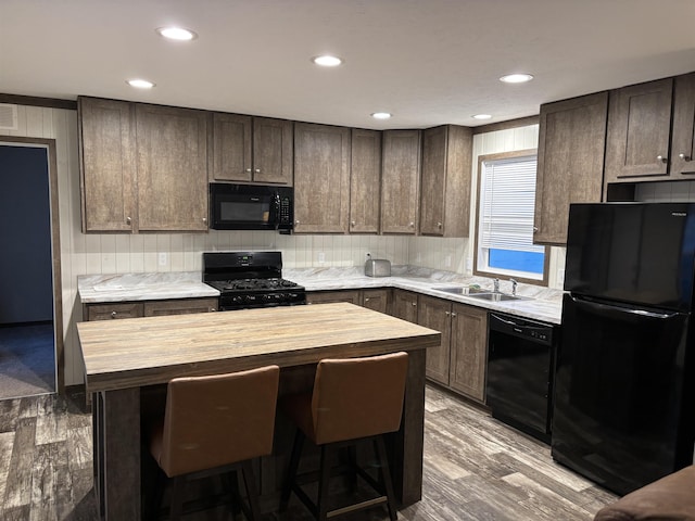 kitchen with a kitchen island, a sink, black appliances, dark brown cabinets, and wood counters