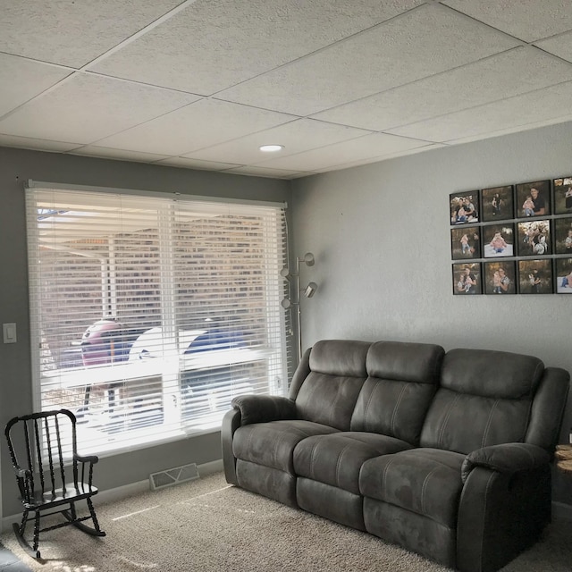 living area featuring carpet floors, visible vents, a drop ceiling, and a wealth of natural light