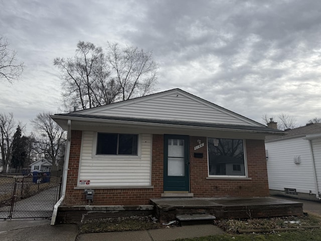 bungalow-style home with covered porch, brick siding, and fence