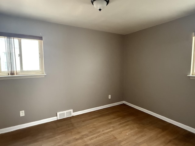 unfurnished room featuring wood finished floors, visible vents, and baseboards