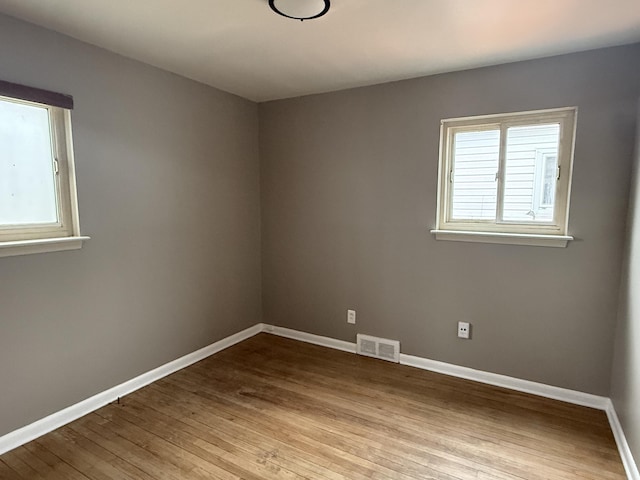 spare room featuring wood finished floors, visible vents, and baseboards