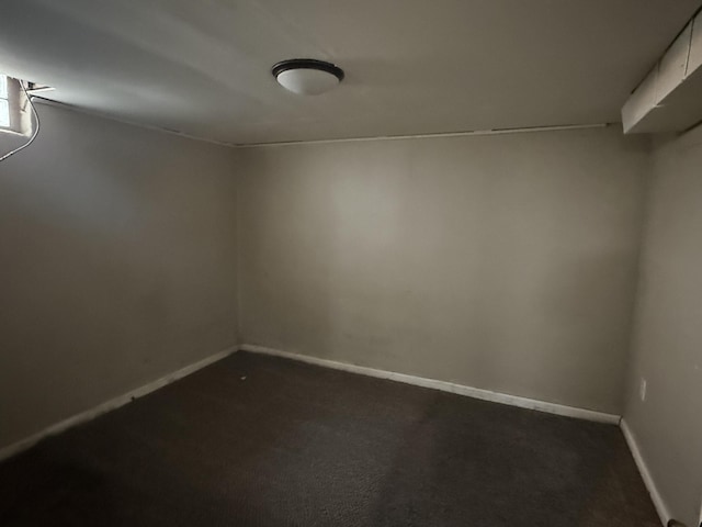 unfurnished room featuring dark colored carpet and baseboards