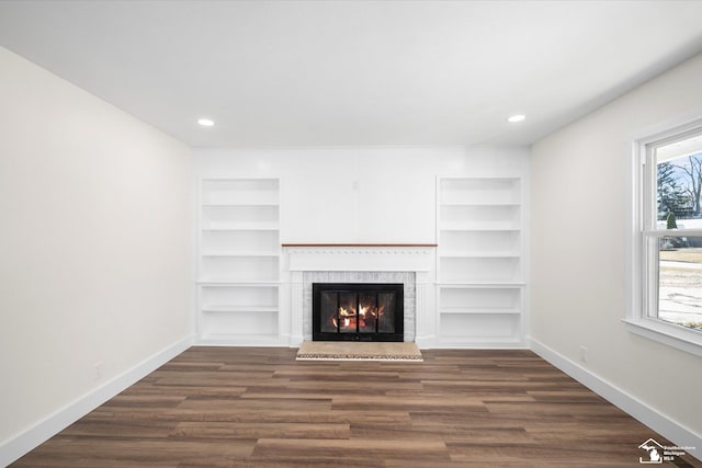 unfurnished living room with a lit fireplace, dark wood-type flooring, recessed lighting, and baseboards