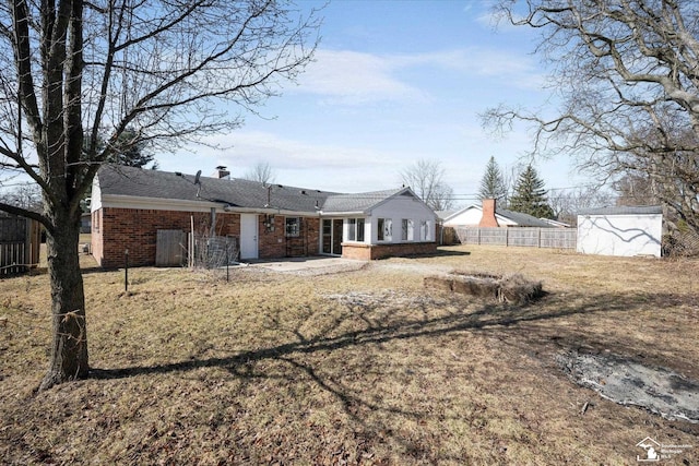 rear view of house featuring a patio area, brick siding, fence, and a chimney