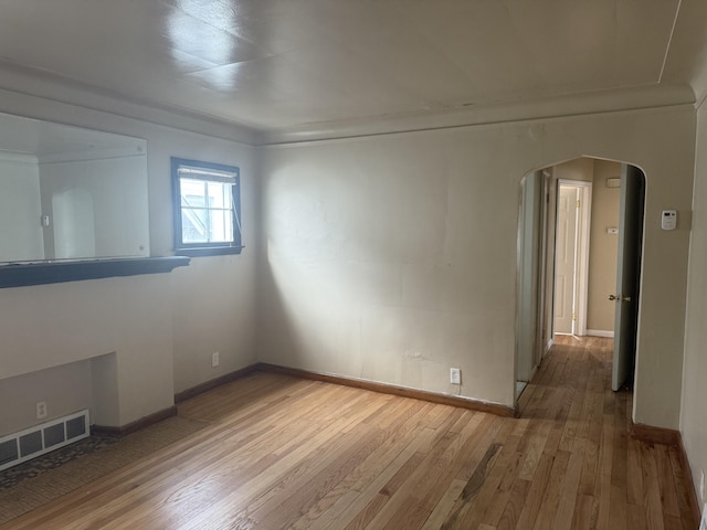 spare room with arched walkways, baseboards, visible vents, and hardwood / wood-style floors