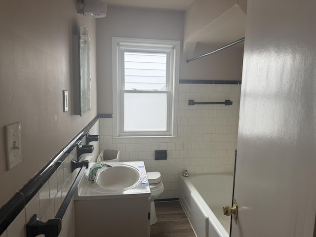 bathroom featuring wainscoting, toilet, wood finished floors, vanity, and tile walls