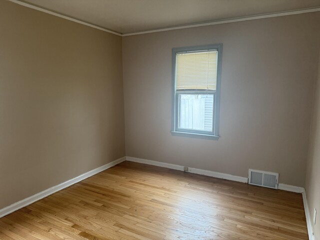 spare room with ornamental molding, light wood finished floors, visible vents, and baseboards