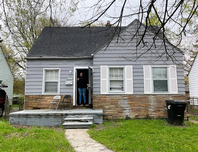 view of front facade with stone siding, a shingled roof, a chimney, and a front yard