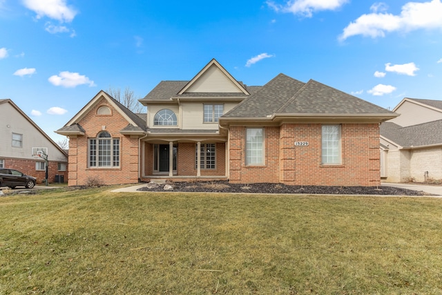 traditional home featuring a shingled roof, a front yard, and brick siding