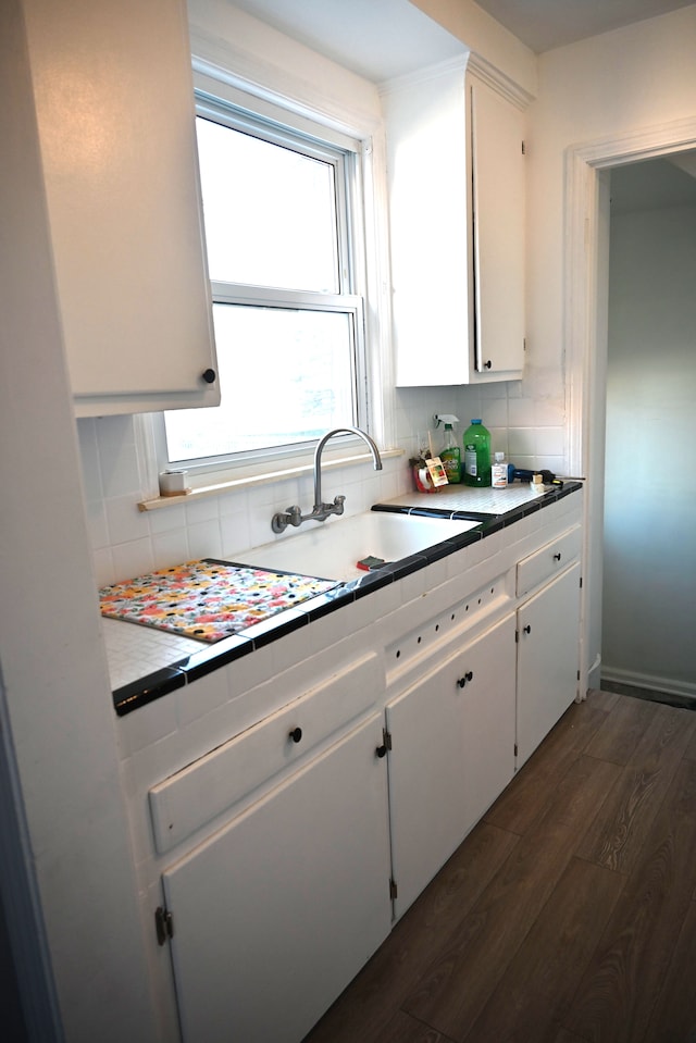 kitchen featuring dark wood-type flooring, a sink, white cabinetry, and decorative backsplash