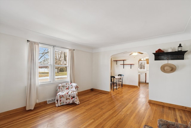 living area with visible vents, arched walkways, light wood-style floors, and baseboards