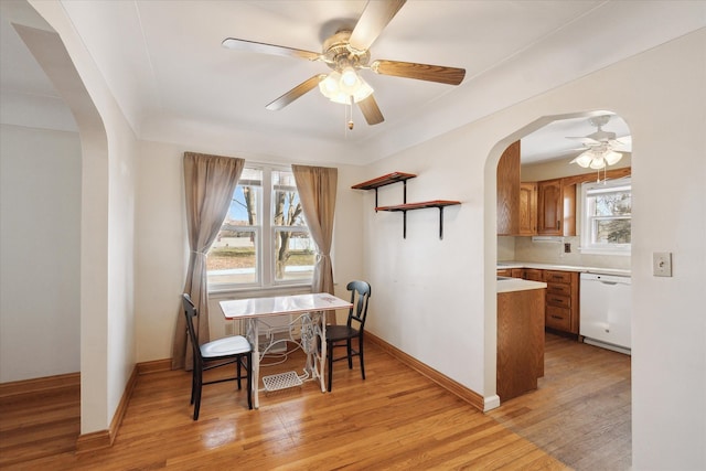 dining room featuring arched walkways, a healthy amount of sunlight, light wood-type flooring, and baseboards