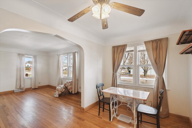 dining room featuring arched walkways, ceiling fan, baseboards, and light wood-style floors