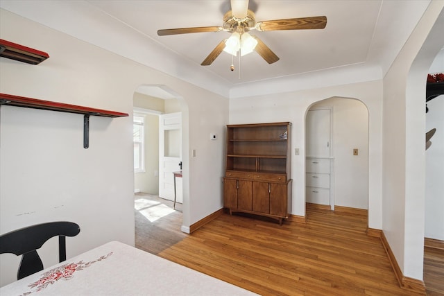 bedroom featuring a ceiling fan, wood finished floors, baseboards, arched walkways, and a closet