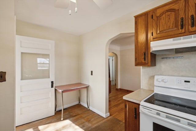 kitchen with brown cabinetry, white electric range, arched walkways, and under cabinet range hood