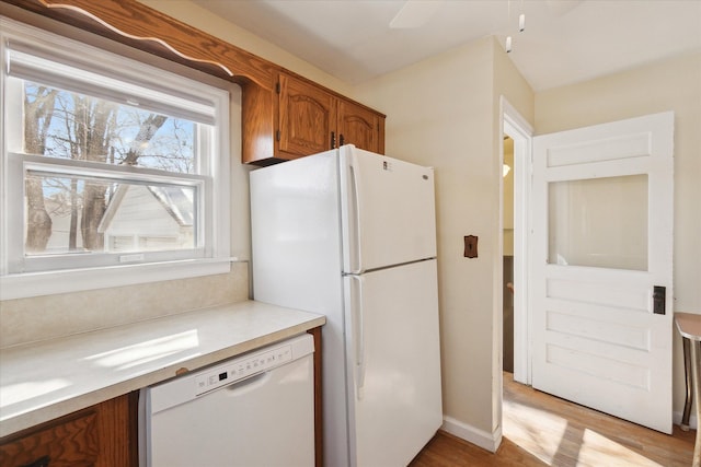 kitchen with brown cabinets, light wood-style flooring, a ceiling fan, white appliances, and light countertops