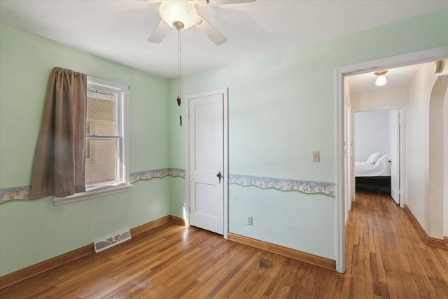 unfurnished bedroom with arched walkways, visible vents, wood-type flooring, and baseboards