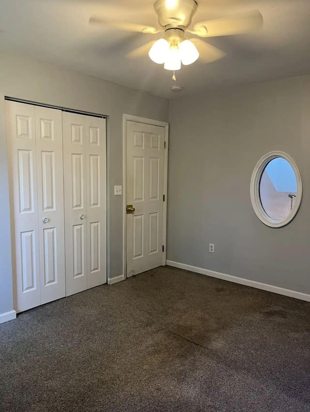 unfurnished bedroom with baseboards, dark carpet, ceiling fan, and a closet