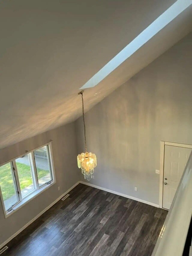 interior space with vaulted ceiling with skylight, dark wood-type flooring, and baseboards