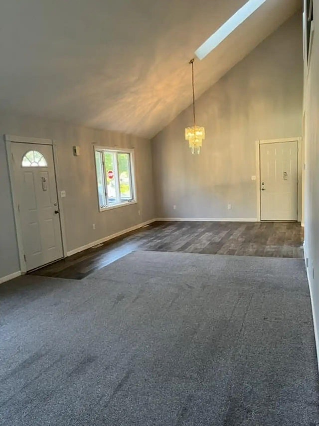 foyer entrance with high vaulted ceiling, a skylight, baseboards, dark colored carpet, and an inviting chandelier