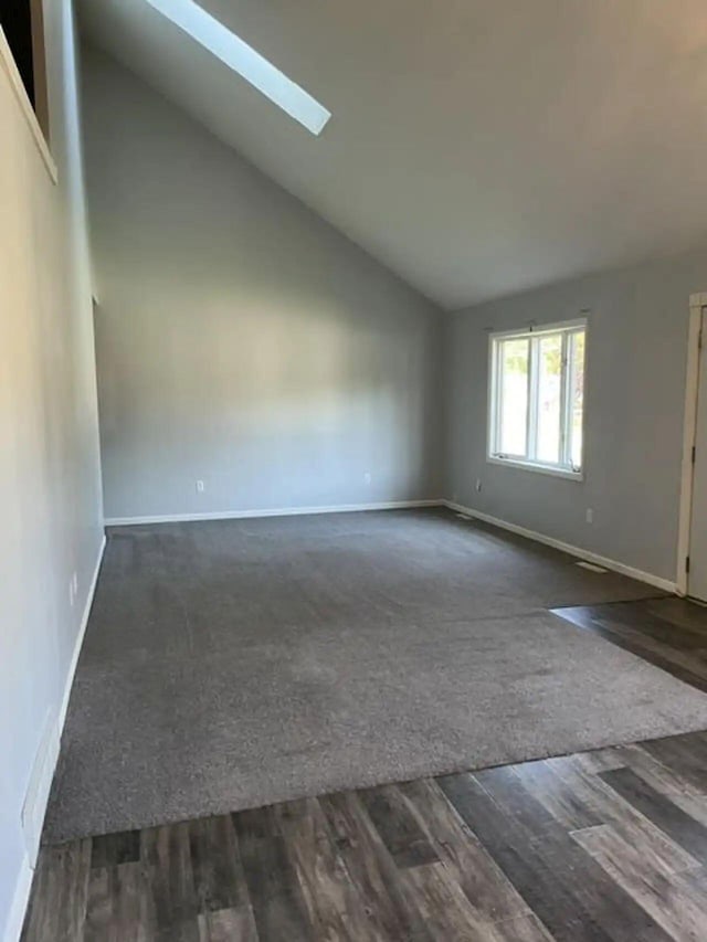 unfurnished room with dark wood-style floors, high vaulted ceiling, a skylight, and baseboards