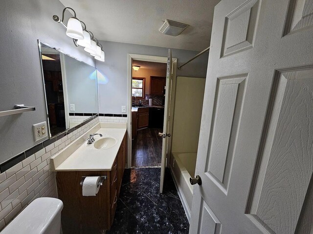 full bath with a wainscoted wall, visible vents, tile walls, and vanity