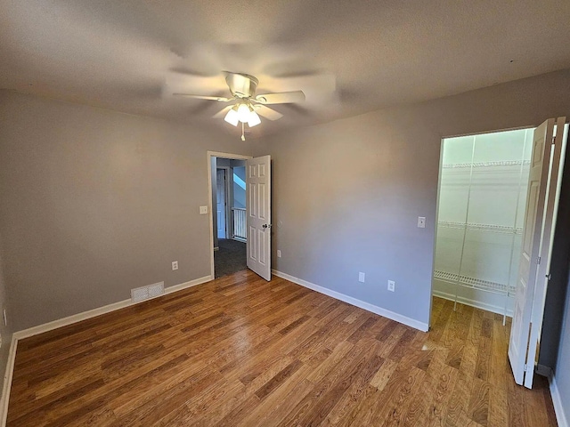 unfurnished bedroom featuring a walk in closet, visible vents, baseboards, and wood finished floors