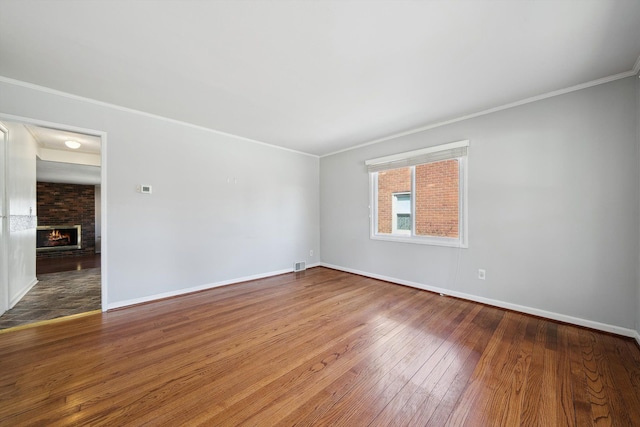 spare room with a brick fireplace, baseboards, wood-type flooring, and ornamental molding