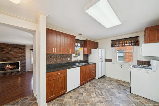 kitchen featuring white appliances, a sink, stone finish floor, dark countertops, and a brick fireplace