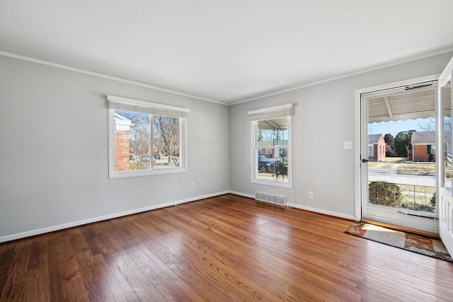 empty room with visible vents, wood-type flooring, baseboards, and crown molding