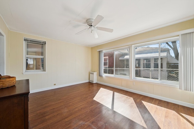 empty room featuring radiator heating unit, wood finished floors, baseboards, and ceiling fan