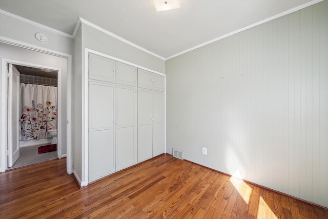 unfurnished bedroom featuring visible vents, a closet, wood finished floors, and ornamental molding