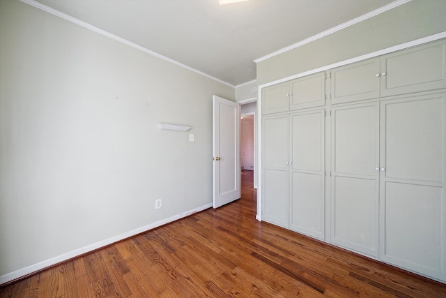 unfurnished bedroom with a closet, crown molding, baseboards, and wood finished floors