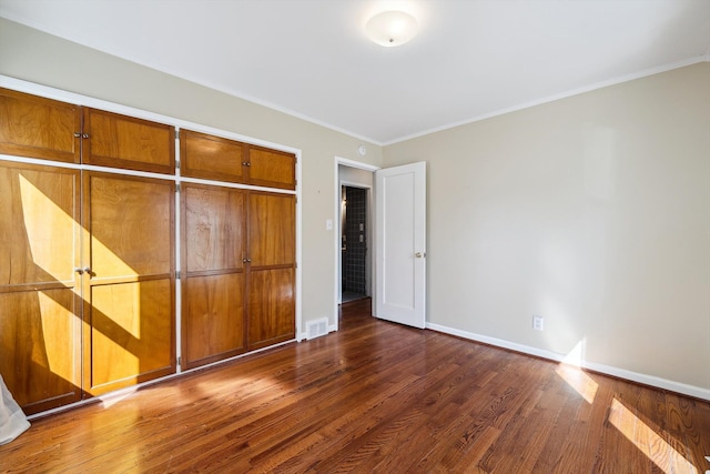 unfurnished bedroom with wood finished floors, visible vents, baseboards, a closet, and crown molding