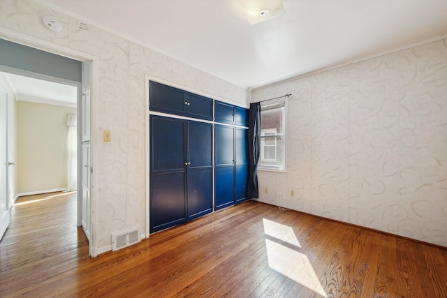 unfurnished bedroom with visible vents, wood-type flooring, a closet, and ornamental molding