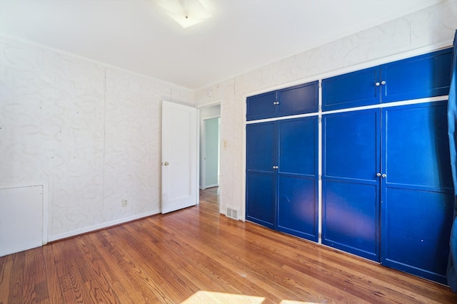 unfurnished bedroom with visible vents, ornamental molding, baseboards, and wood finished floors